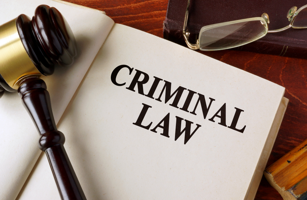 Book with title criminal law on a table. Open book that says criminal law underneath gavel and next to glasses